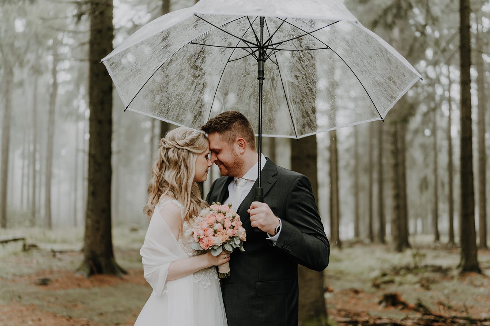 Brautpaar Christian und Stefanie unter transparentem Regenschirm im Wald